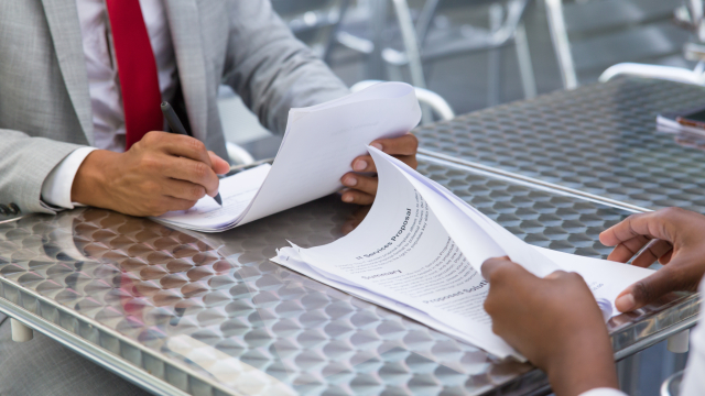 Business partners checking and signing documents in street cafe. Closeup of papers and writing business man hand. Deal or paperwork concept